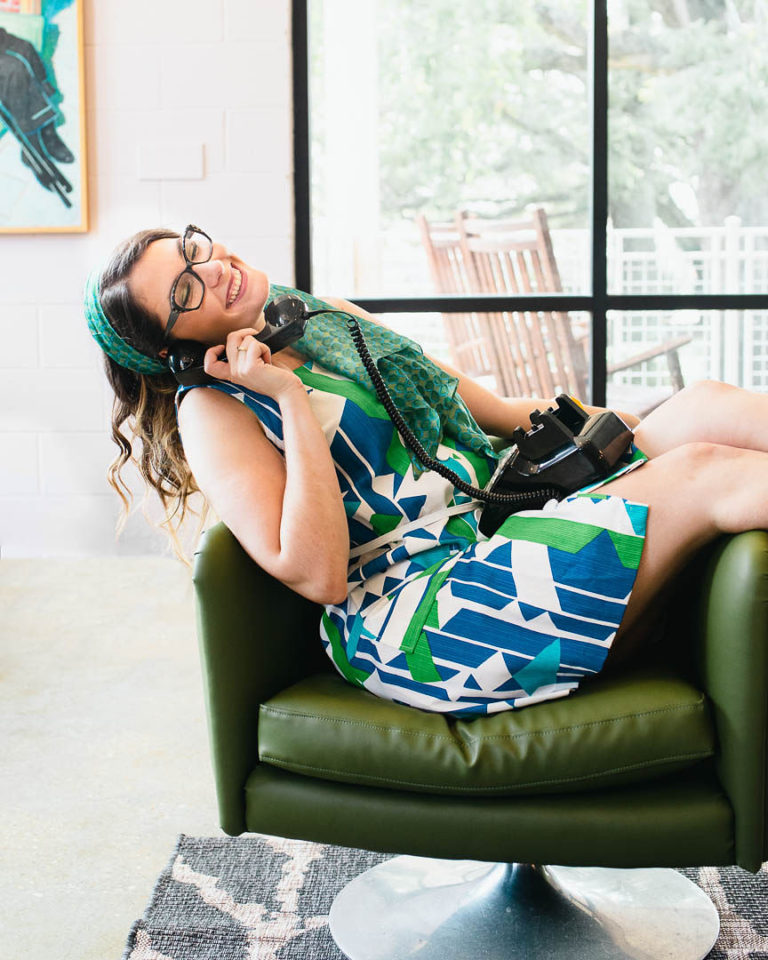 Samm Sawyer sitting in a chair answering a rotary phone in vintage clothes, smiling